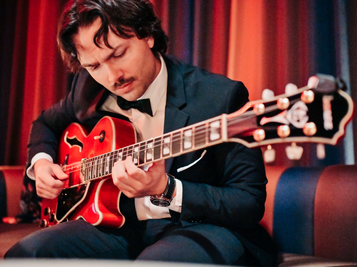 Chase Maddox playing his red archtop guitar in a tuxedo